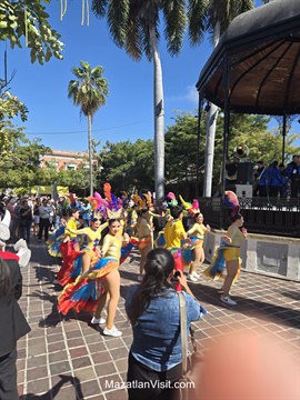 Vibrant live performance dancers moving past packed outdoor dining terraces during opening day