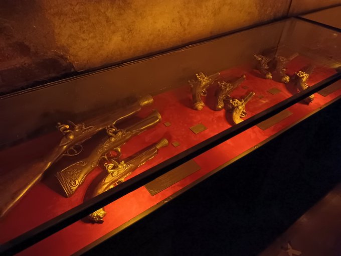 Detailed replica flintlock weapons and historical pirate flags hanging on stone walls
